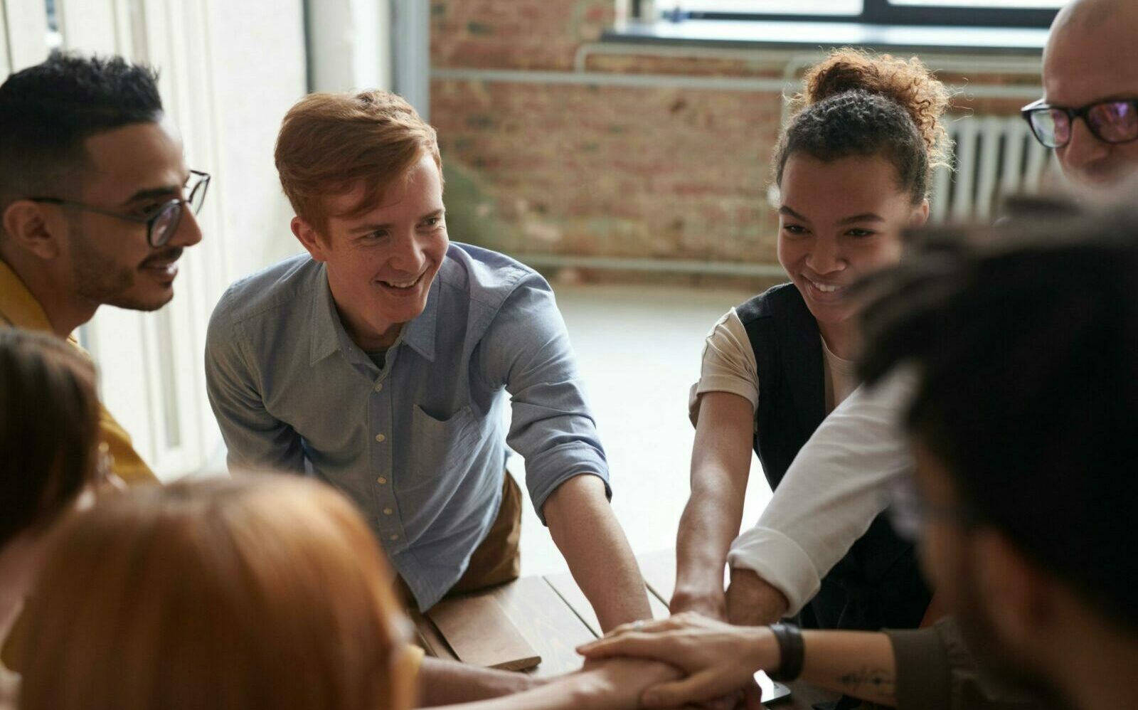 A diverse group of young professionals joining hands in a cheerful and supportive team-building activity.